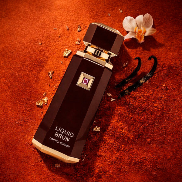 French Avenue Liquid Brun Limited Edition 150ml Extrait de Parfum bottle in brown and gold, styled on a warm terracotta background with gold flakes, an orchid, and vanilla pods.